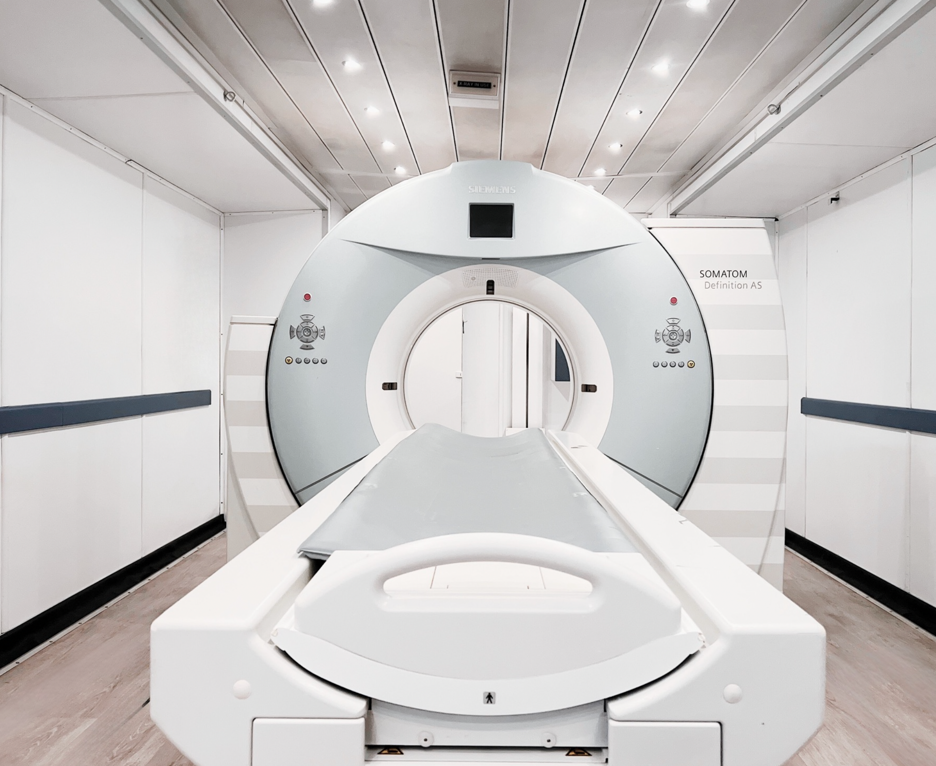 Medical CT scanner in a bright white hospital room with a patient table extending into the machine