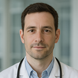 Portrait of a doctor in a white coat and stethoscope, looking at the camera in a bright clinic
