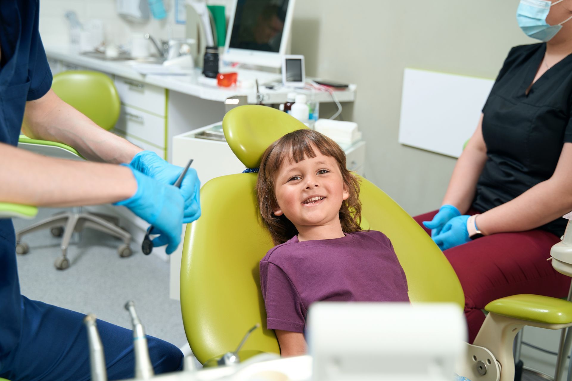 Child sitting in dental chair while pediatric dentist prepares tools for a routine checkup. Child sitting in dental chair while pediatric dentist prepares tools for a routine checkup.