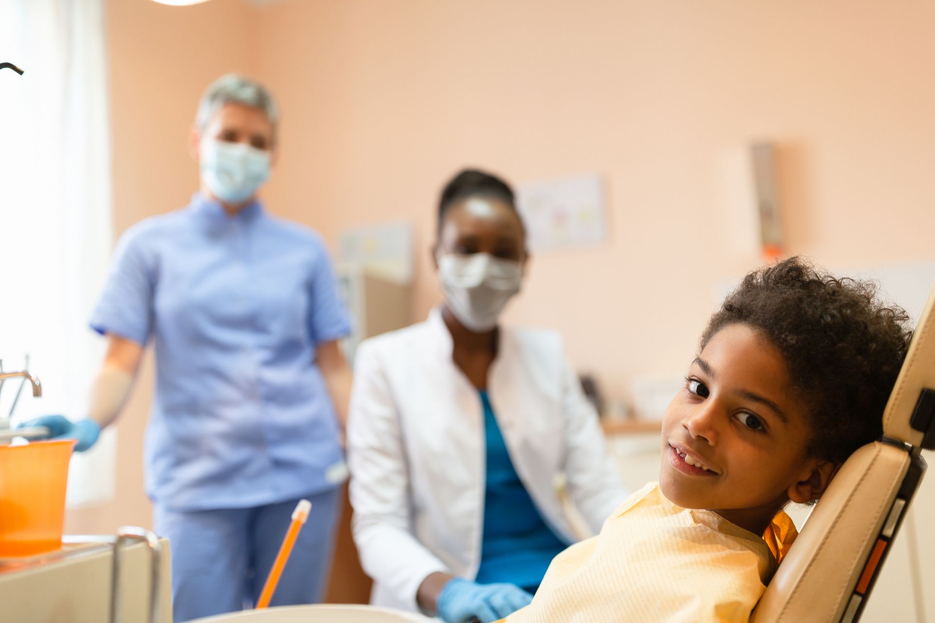 Smiling child in dental chair with two masked dentists | Pediatric Dentist | Kodiak, AK
