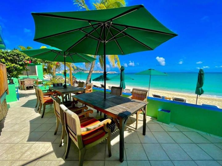 Patio dining tables with green umbrellas overlooking a turquoise beach and ocean.