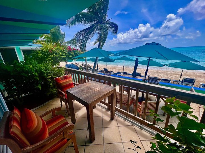Balcony with chairs and table overlooking a beach with umbrellas on a sunny day.