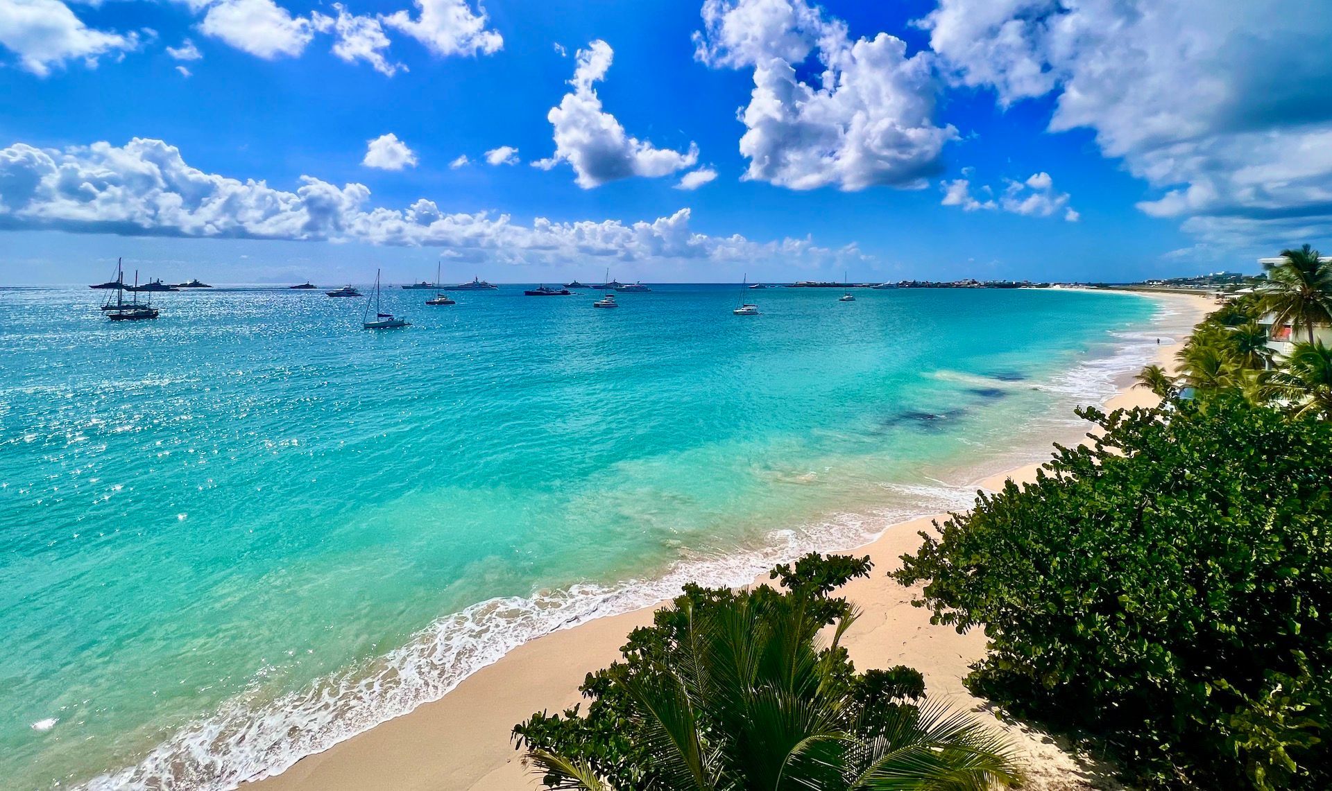 Bright turquoise water meets a white sand beach under a blue sky with puffy clouds.