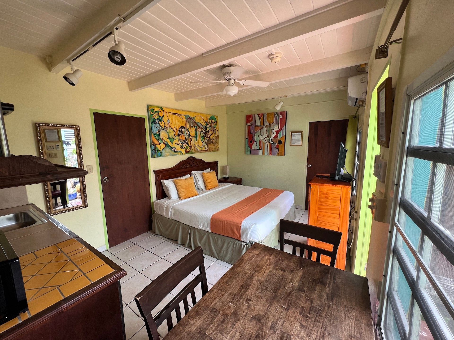 Small studio apartment with bed, table, kitchenette, and artwork.