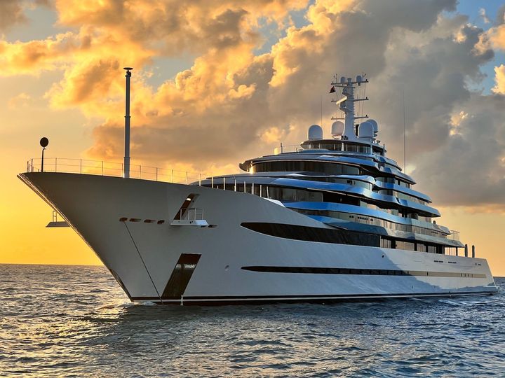 Luxury yacht sailing on ocean at sunset.