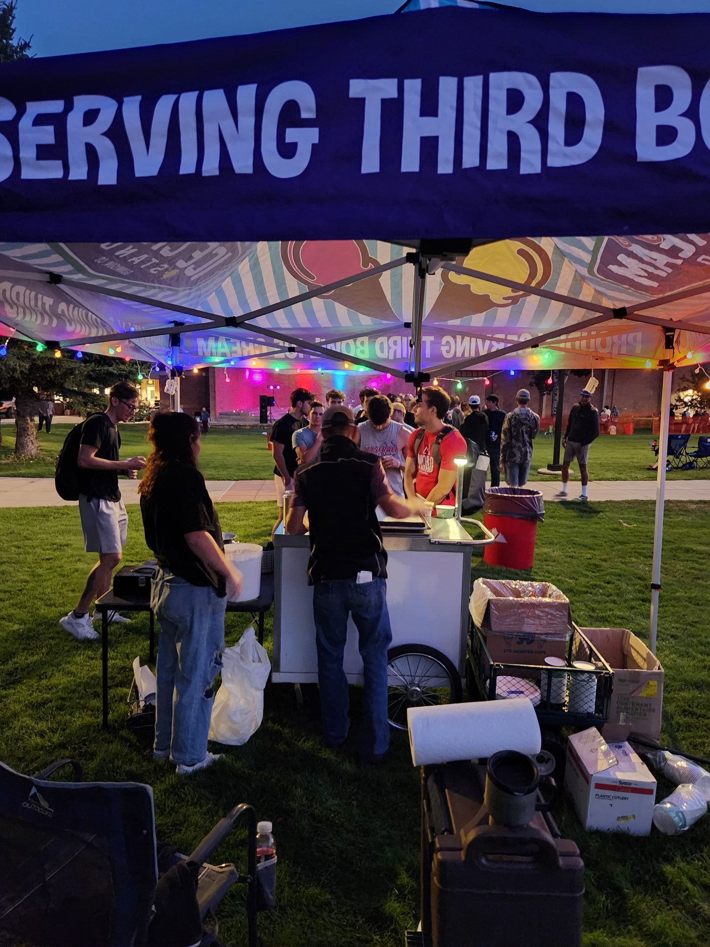 A group of people are standing under a tent that says serving third base.