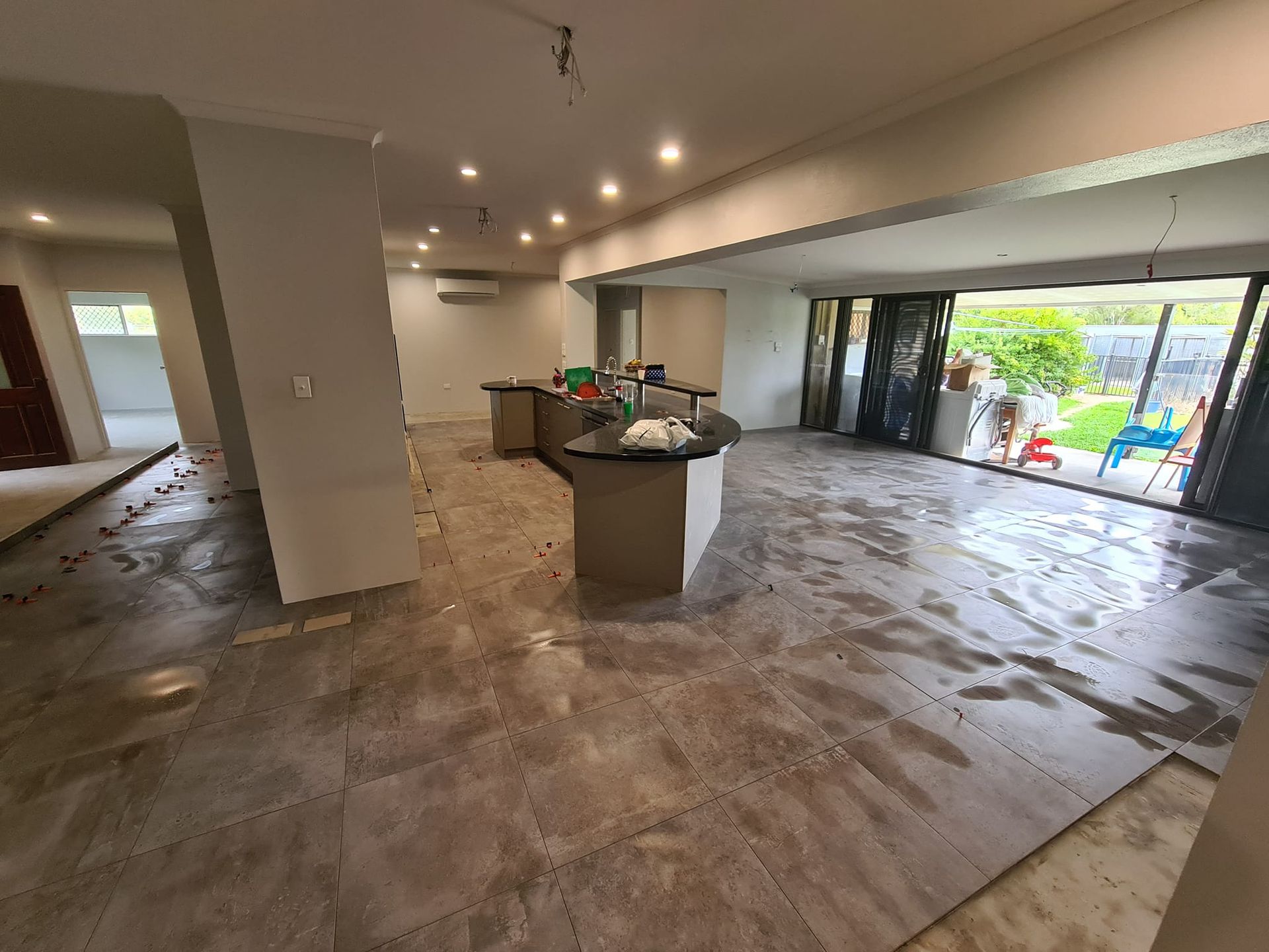 Interior view of a kitchen under renovation, with wet flooring, an island, and open sliding doors — Tropic Tiling in Tolga, QLD