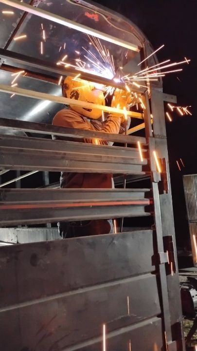 A man is welding a metal structure at night.
