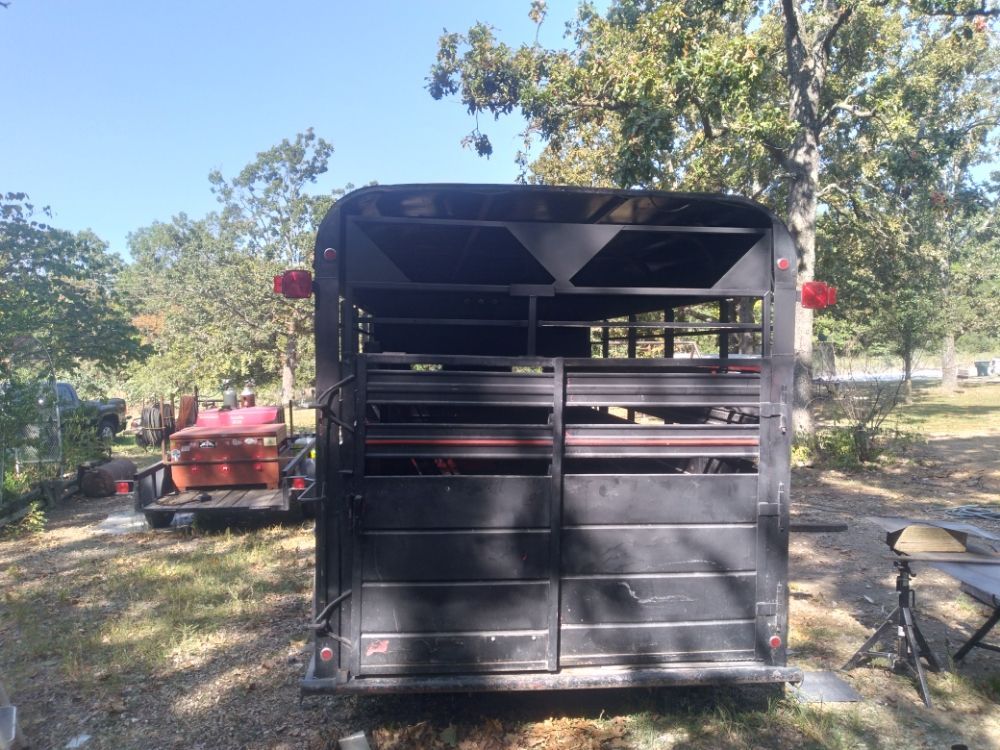 A black trailer is parked in a grassy area with trees in the background.