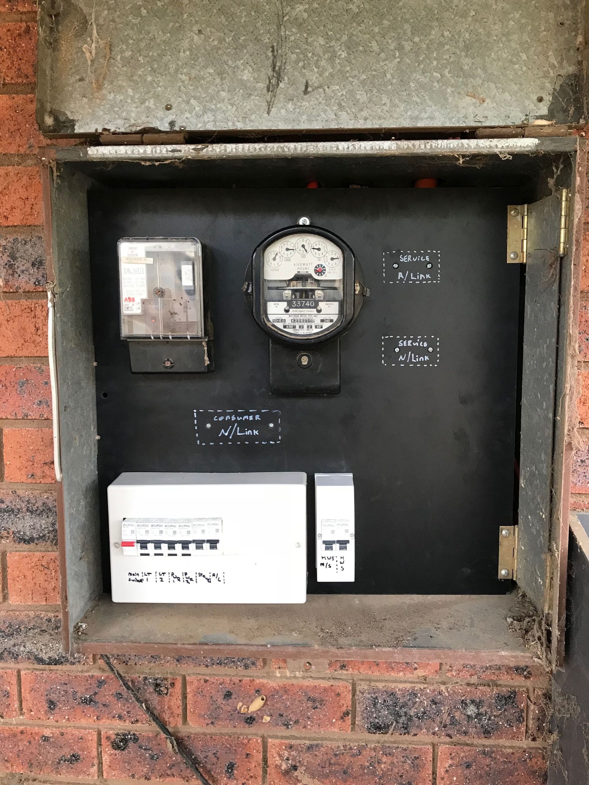 Old electrical meter box set into a brick wall with meters and breaker panel inside