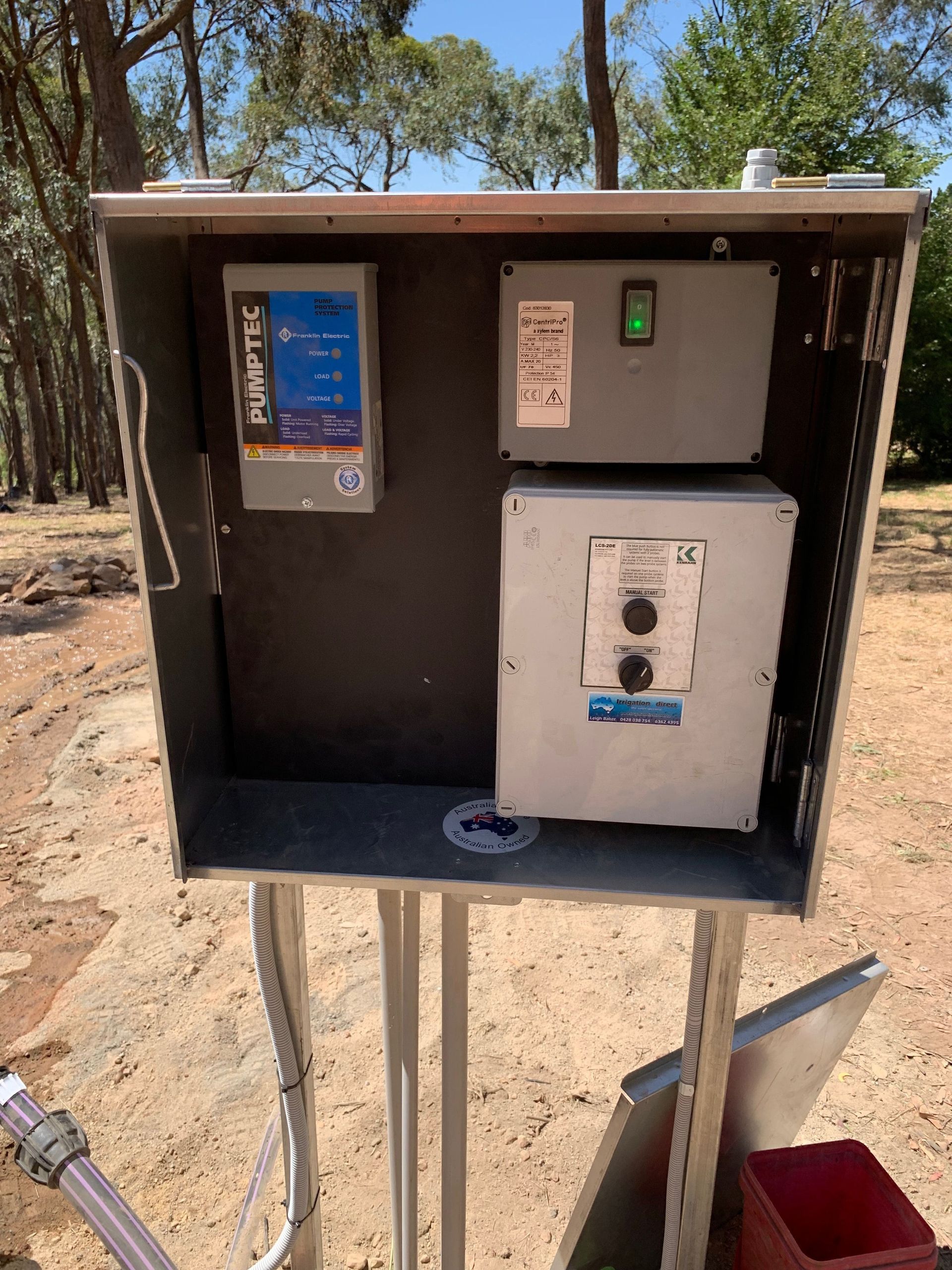 Outdoor electrical control box with switches and meter on metal post, in a dry wooded area