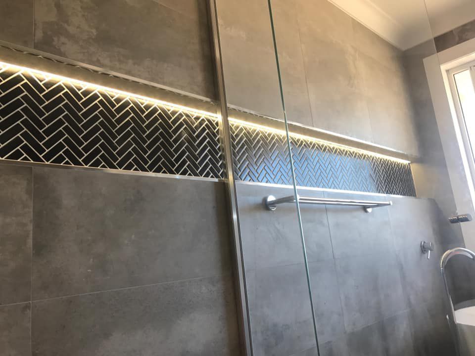 Modern bathroom shower with gray tiles, glass doors, and a black chevron accent strip