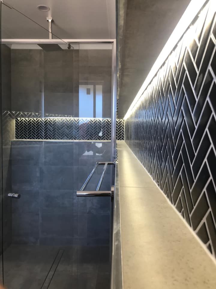 Modern bathroom with glass shower, dark tile, and a black herringbone wall accent.