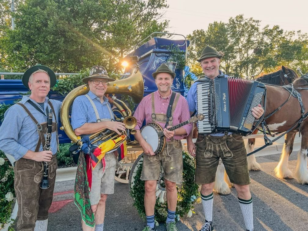 Four musicians pose outdoors at sunset with instruments, including a saxophone and accordion, beside a horse-drawn wagon.