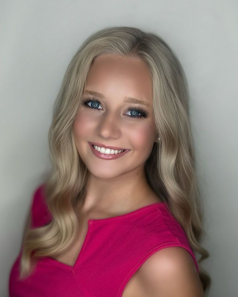 A woman wearing a blue dress and earrings is smiling for the camera.