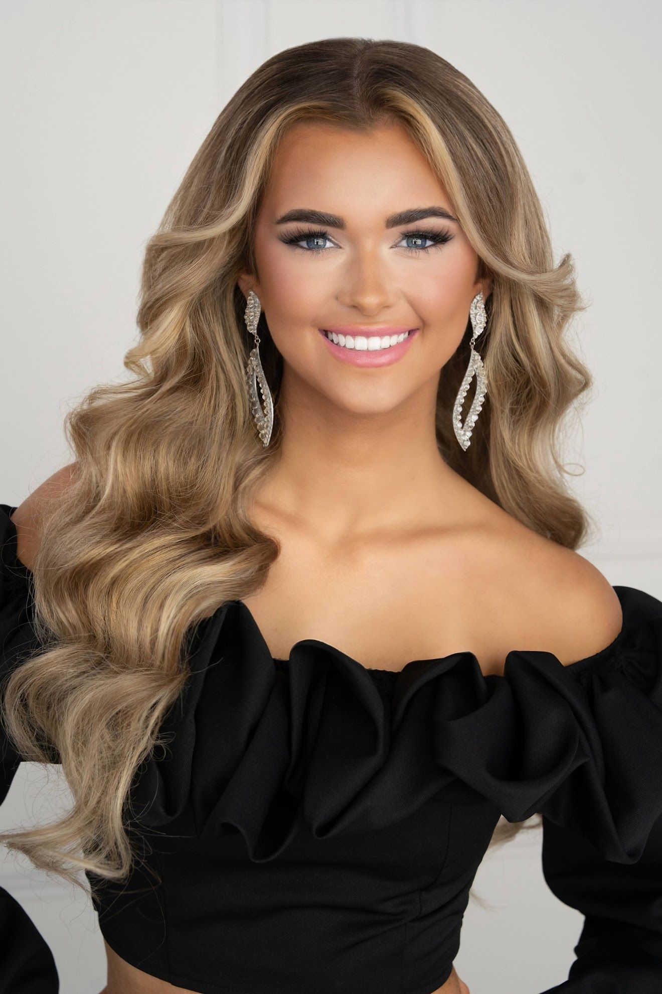 A woman wearing a blue dress and earrings is smiling for the camera.