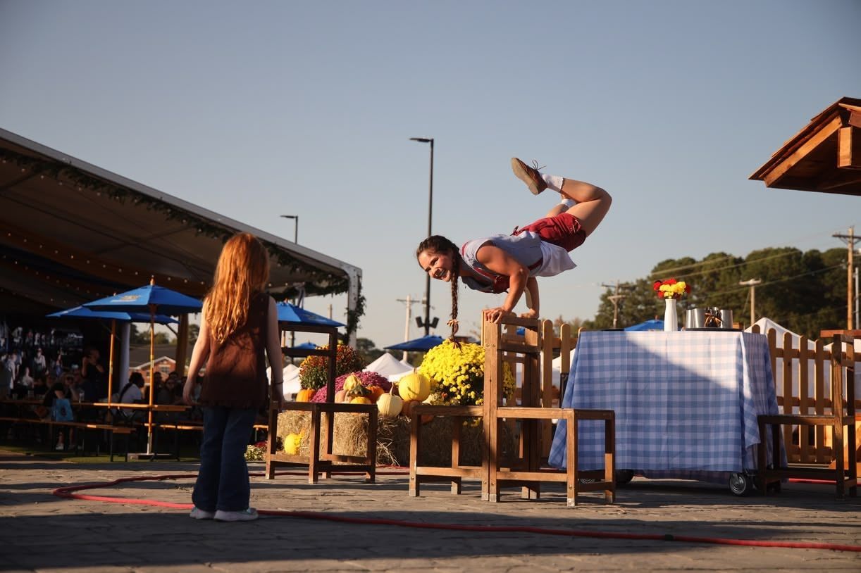 Person mid-flip over wooden benches at an outdoor market or festival at sunset
