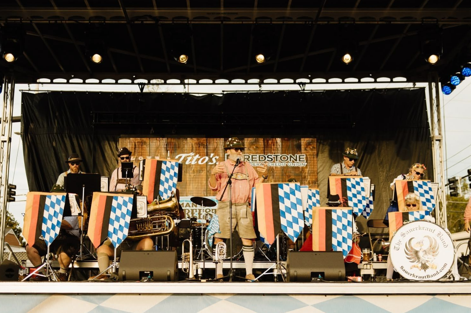 Band performing on an outdoor stage with blue-and-white banners and a drum kit.