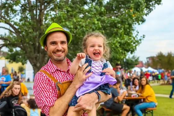 A man is holding a little girl in his arms at a festival.