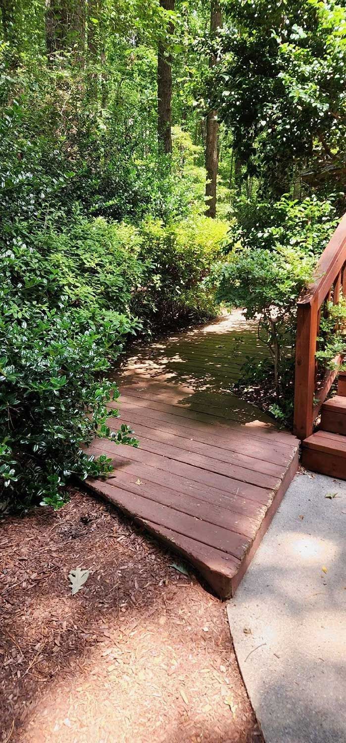 Wooden deck leads to a path through a lush green wooded area.