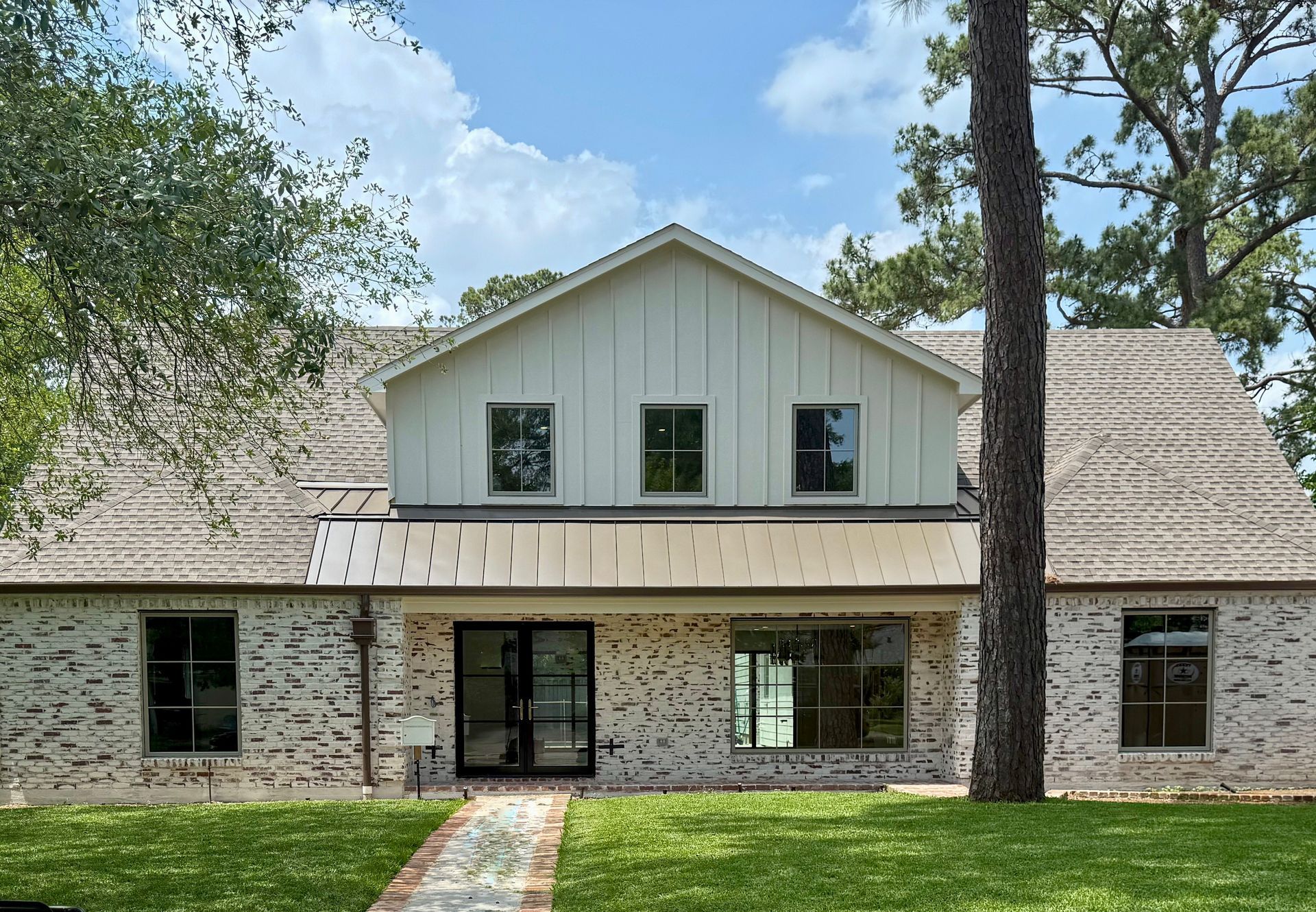 A white brick house with a metal roof and a walkway leading to it.