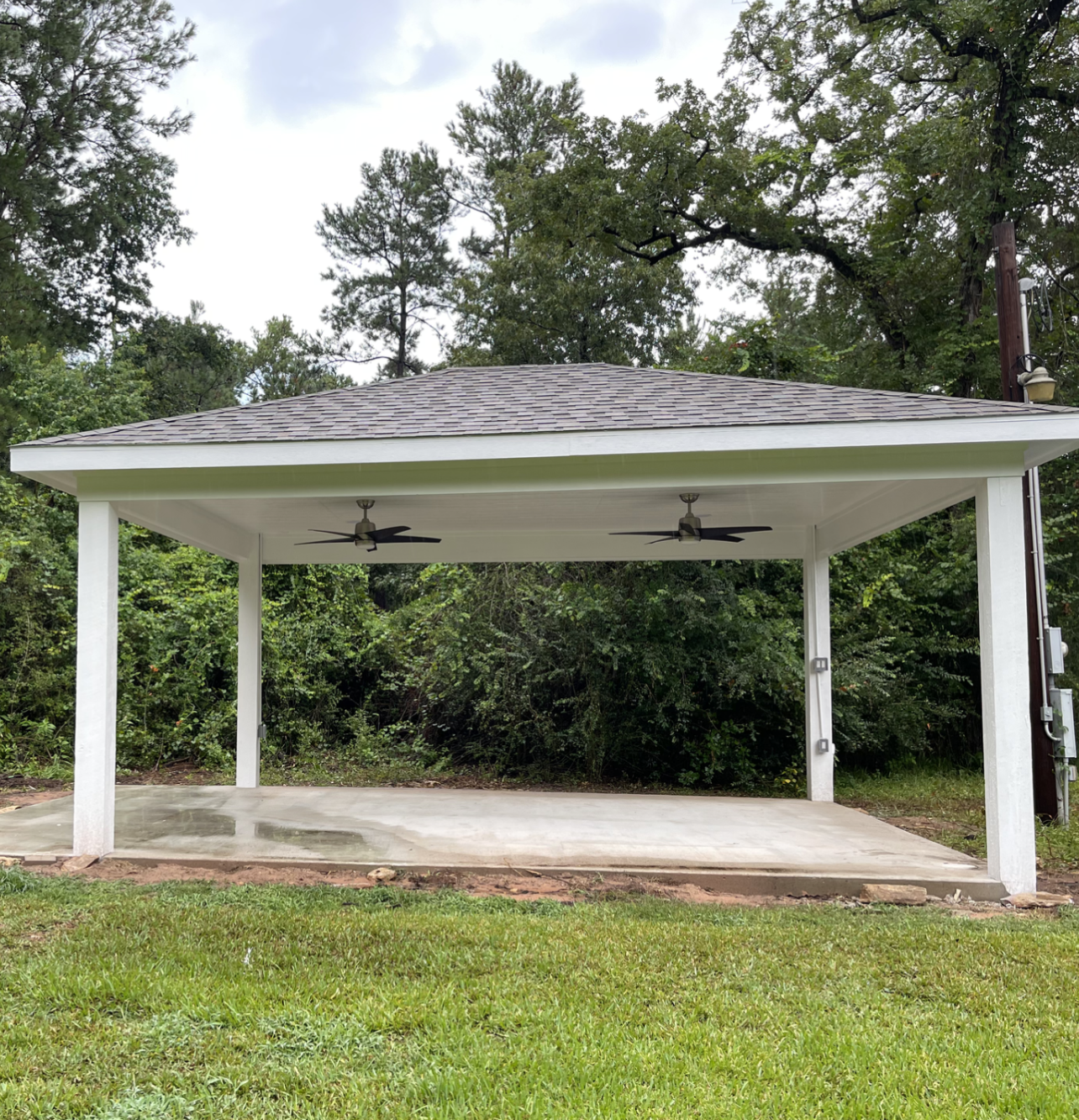 A white pavilion over a concrete patio with two ceiling fans on the roof.