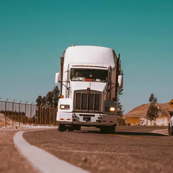 White semi-truck driving on a curving road under a clear blue sky