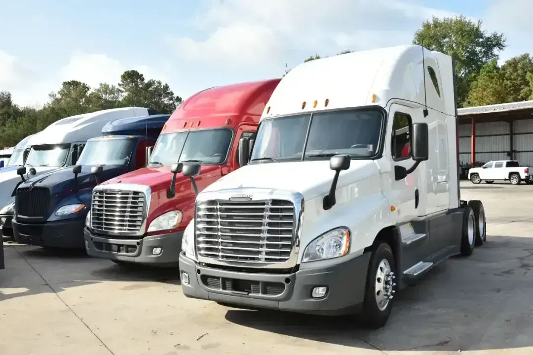 Three semi trucks parked in a lot, including a red and a white truck in front.