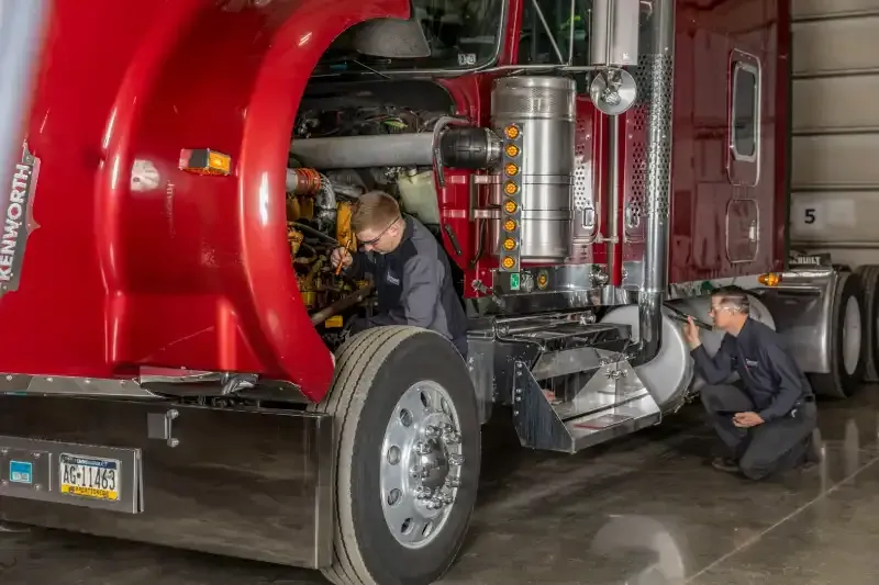 Red truck cab in garage with two workers inspecting the engine and undercarriage