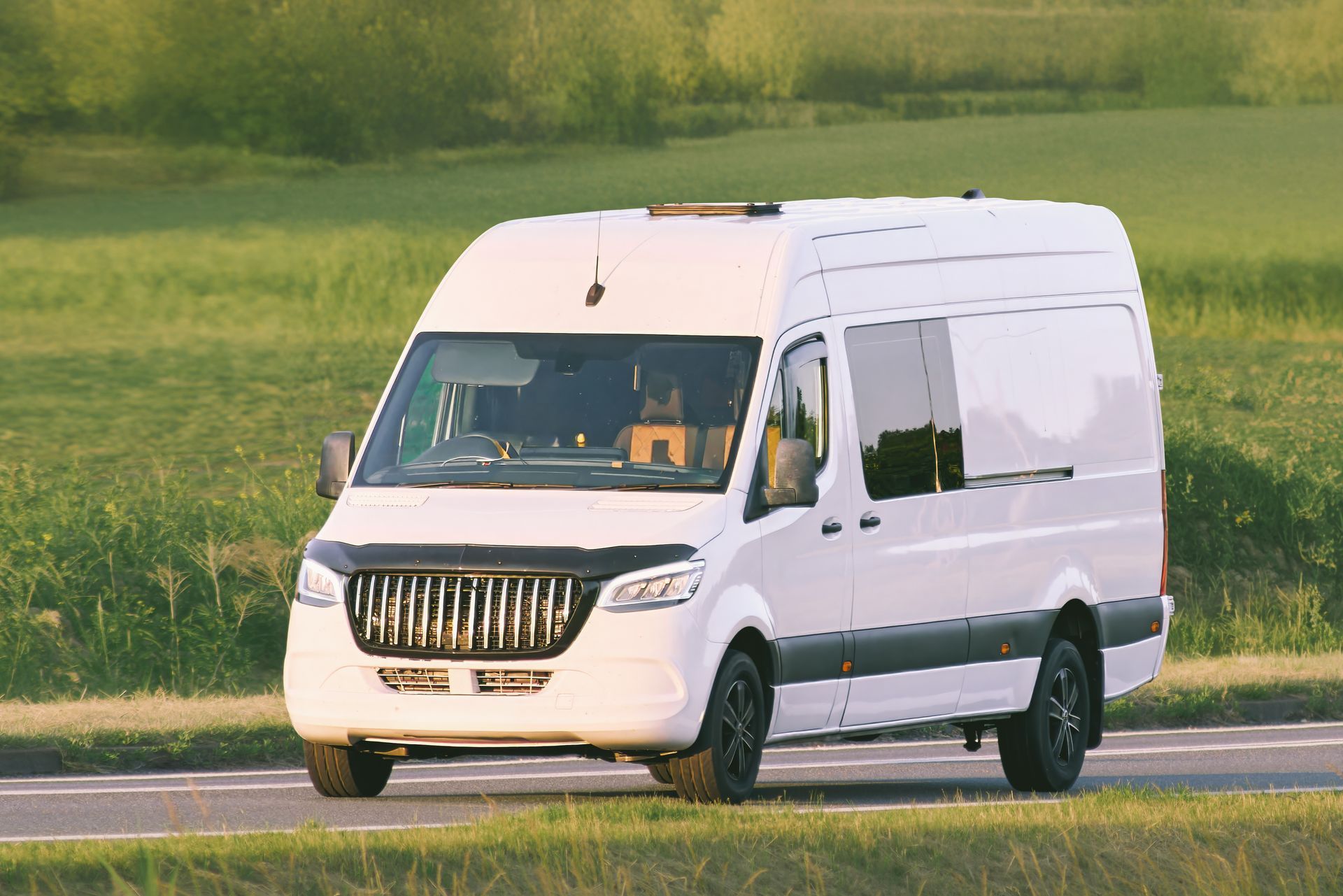 White delivery van driving on a road beside a green field