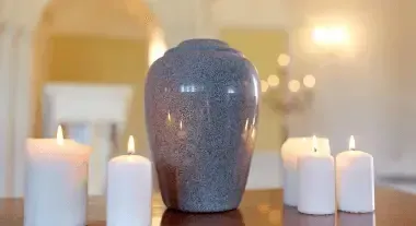 Blue-gray vase centered on a table, surrounded by lit white candles in a softly lit room