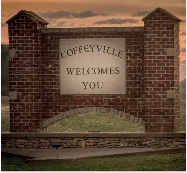 Brick entrance sign reading “Coffeyville Welcomes You” against a cloudy sky.