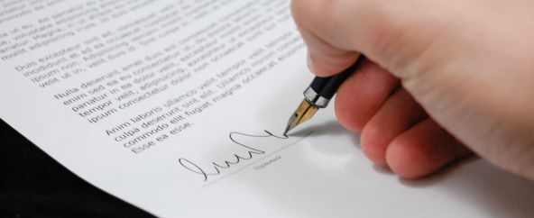 Hand signing a document with a pen on a white page