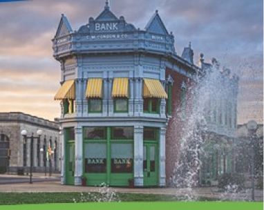 Historic bank building with green awnings beside a fountain at sunset