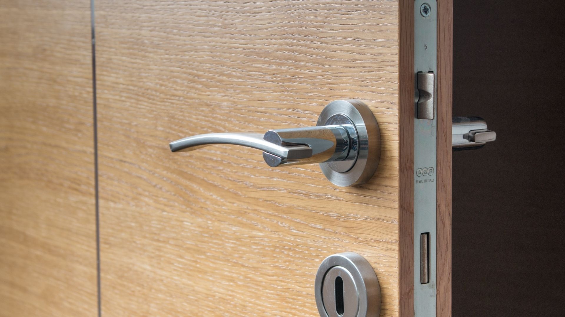 Hands using a screwdriver to repair an old brass door lock on a wooden door
