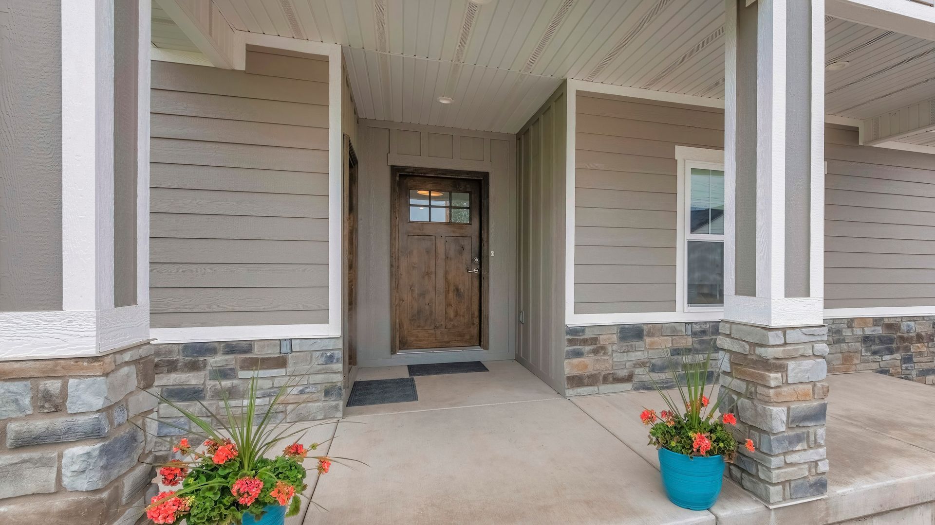 The front porch of a house with a wooden door and a blue pot of flowers.