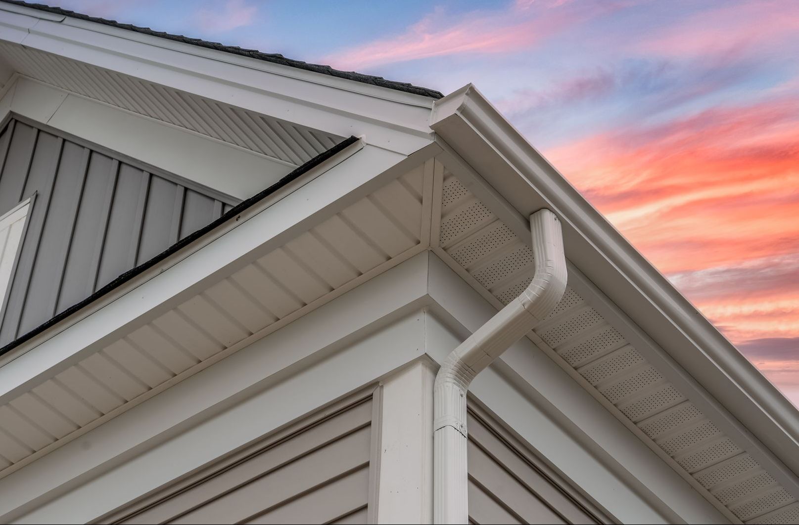 A house with a gutter on the side of it and a sunset in the background.