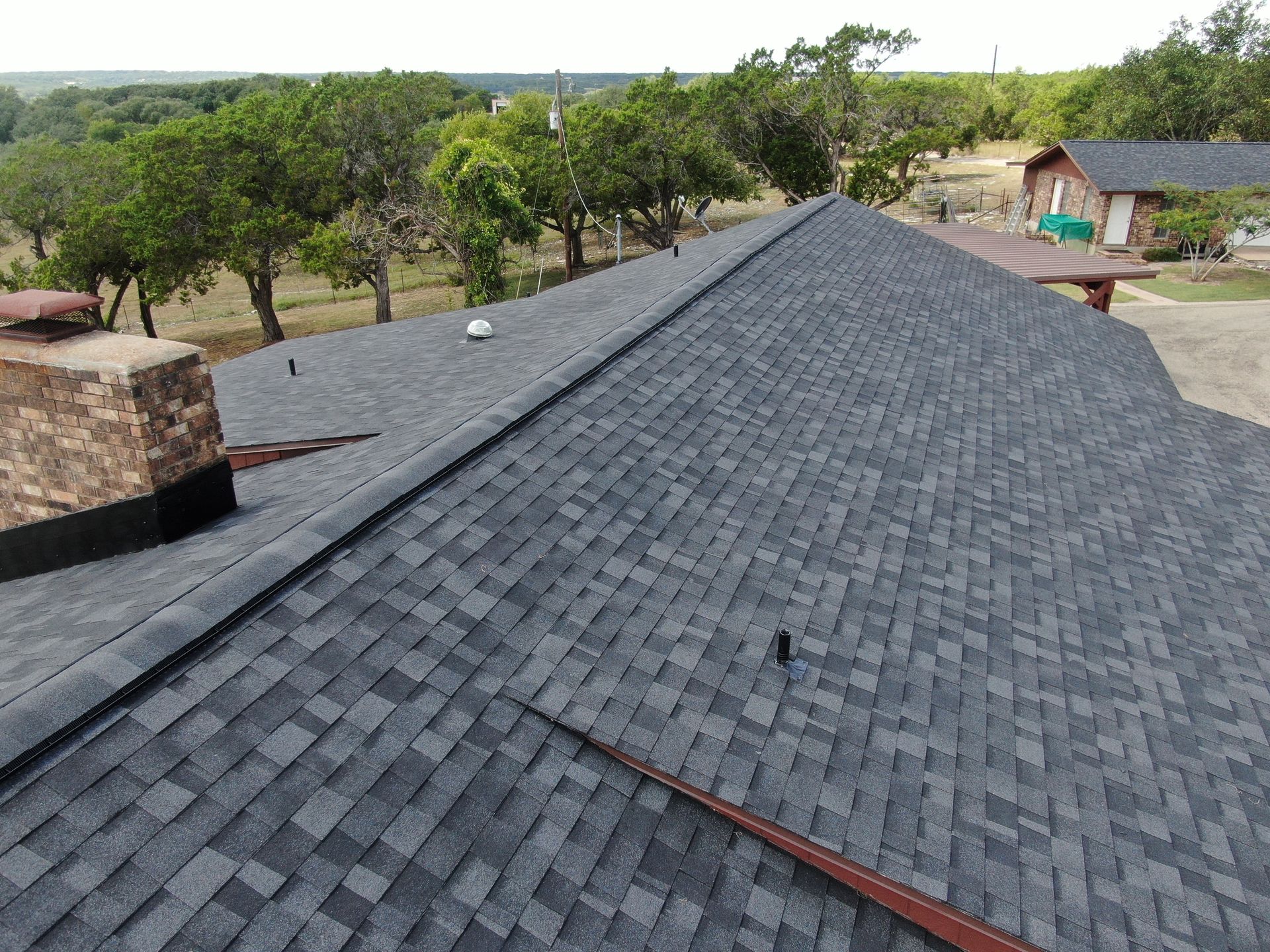 An aerial view of a roof with a chimney and trees in the background.