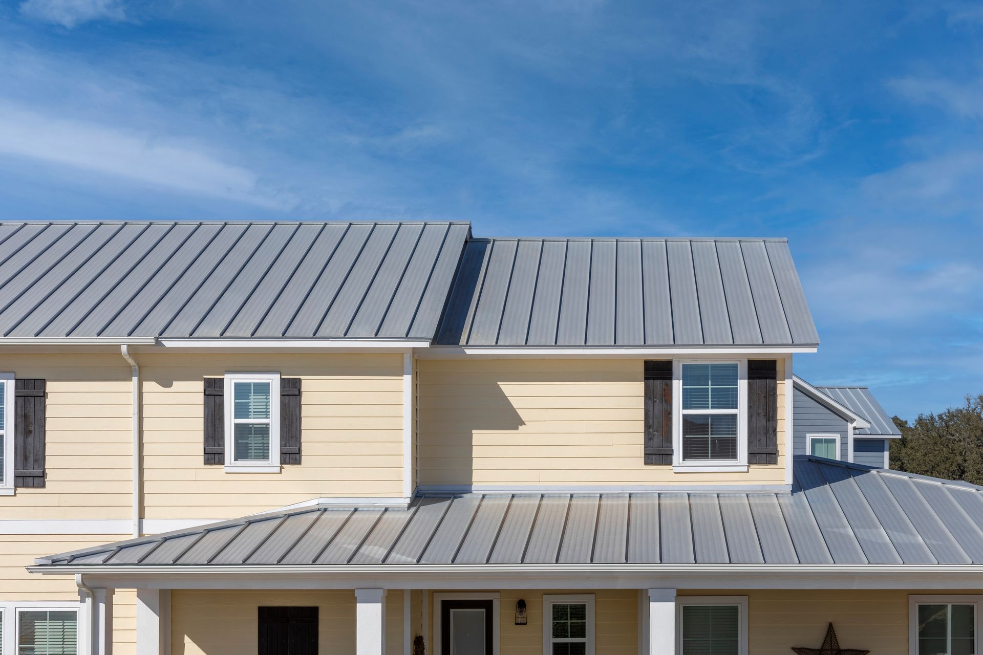A house with a metal roof and black shutters on a sunny day.