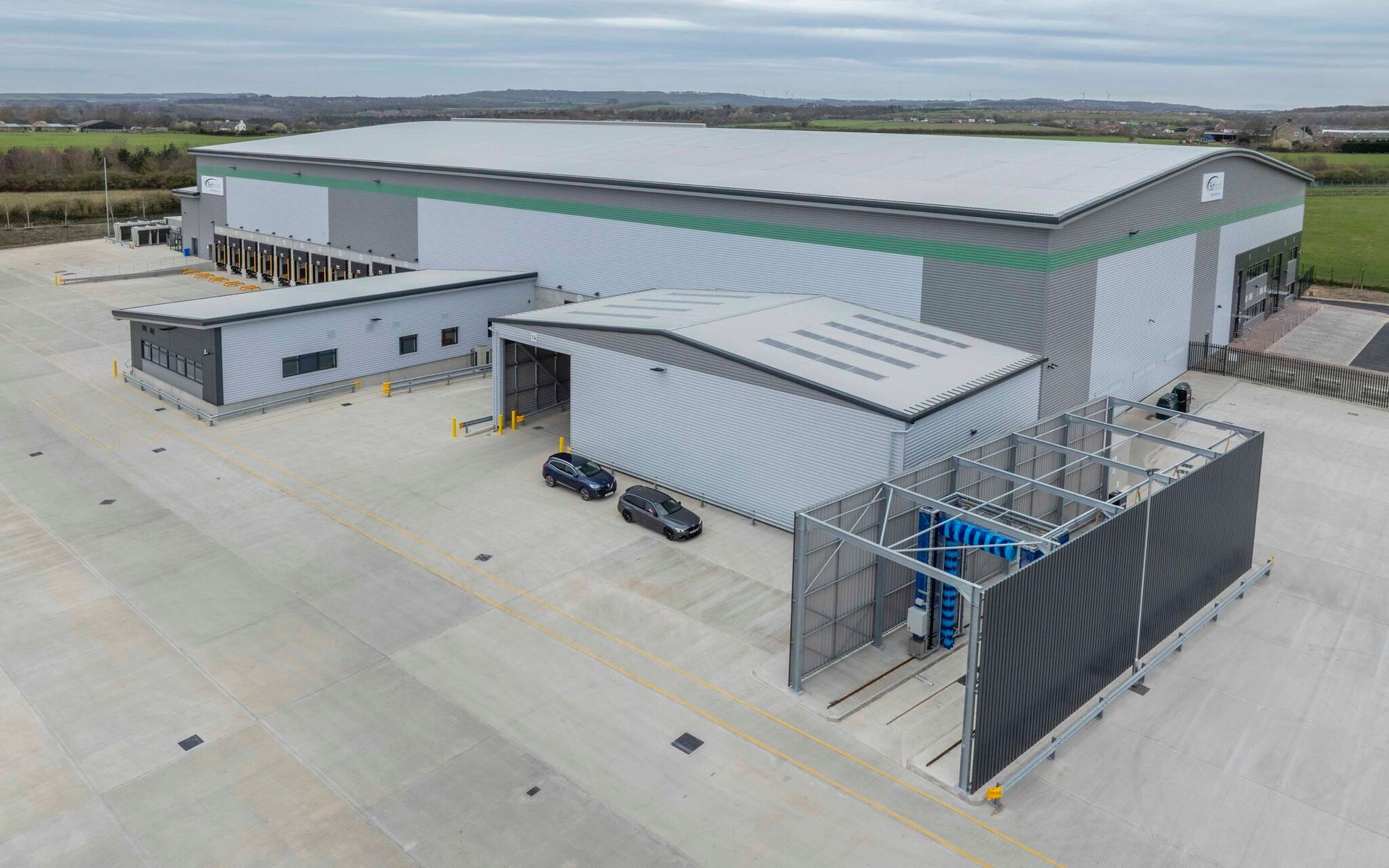 Modern industrial warehouse facility with large loading and parking areas, viewed from a birds eye view exterior on a clear day.
