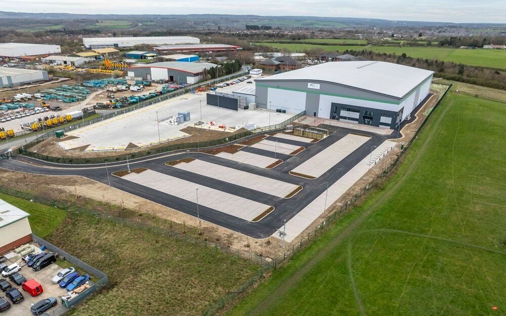 Modern industrial warehouse and office facility with large loading and parking areas, viewed from a birds eye view exterior on a clear day.