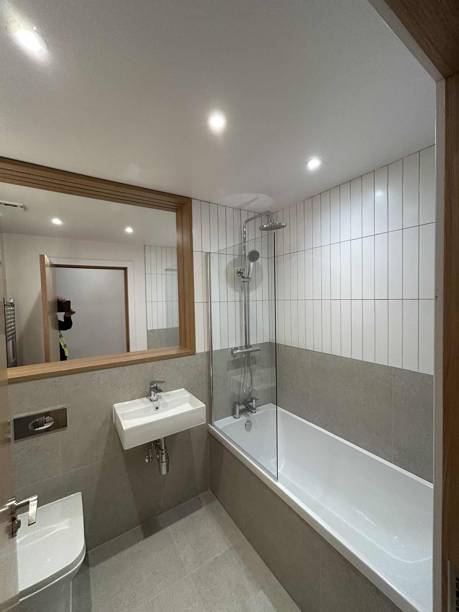 Clean modern bathroom with tiled walls, shower, and large mirror