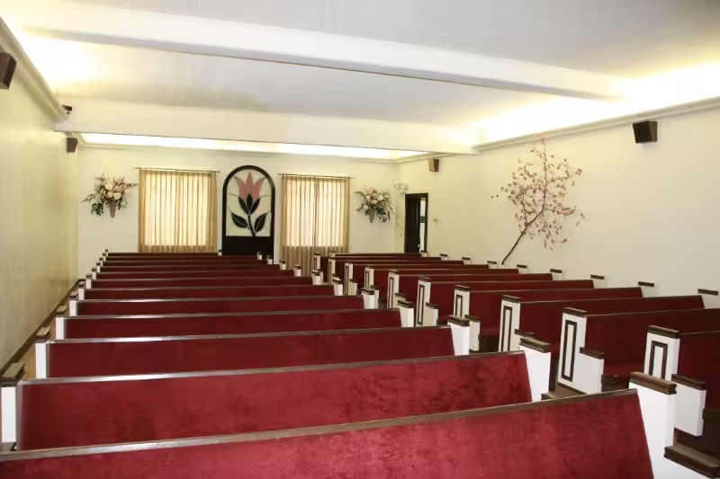 Empty chapel with red pews, white walls, and a central aisle leading to an altar.