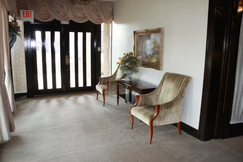 Elegant hotel lobby with chairs, side table, and framed mirror near glass entry doors