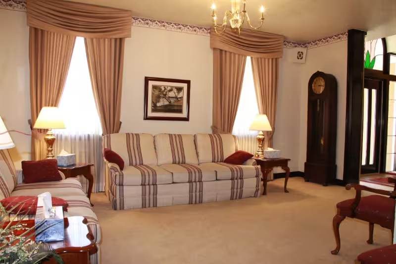 Elegant living room with striped sofa, matching drapes, lamps, and chandelier on a beige carpet