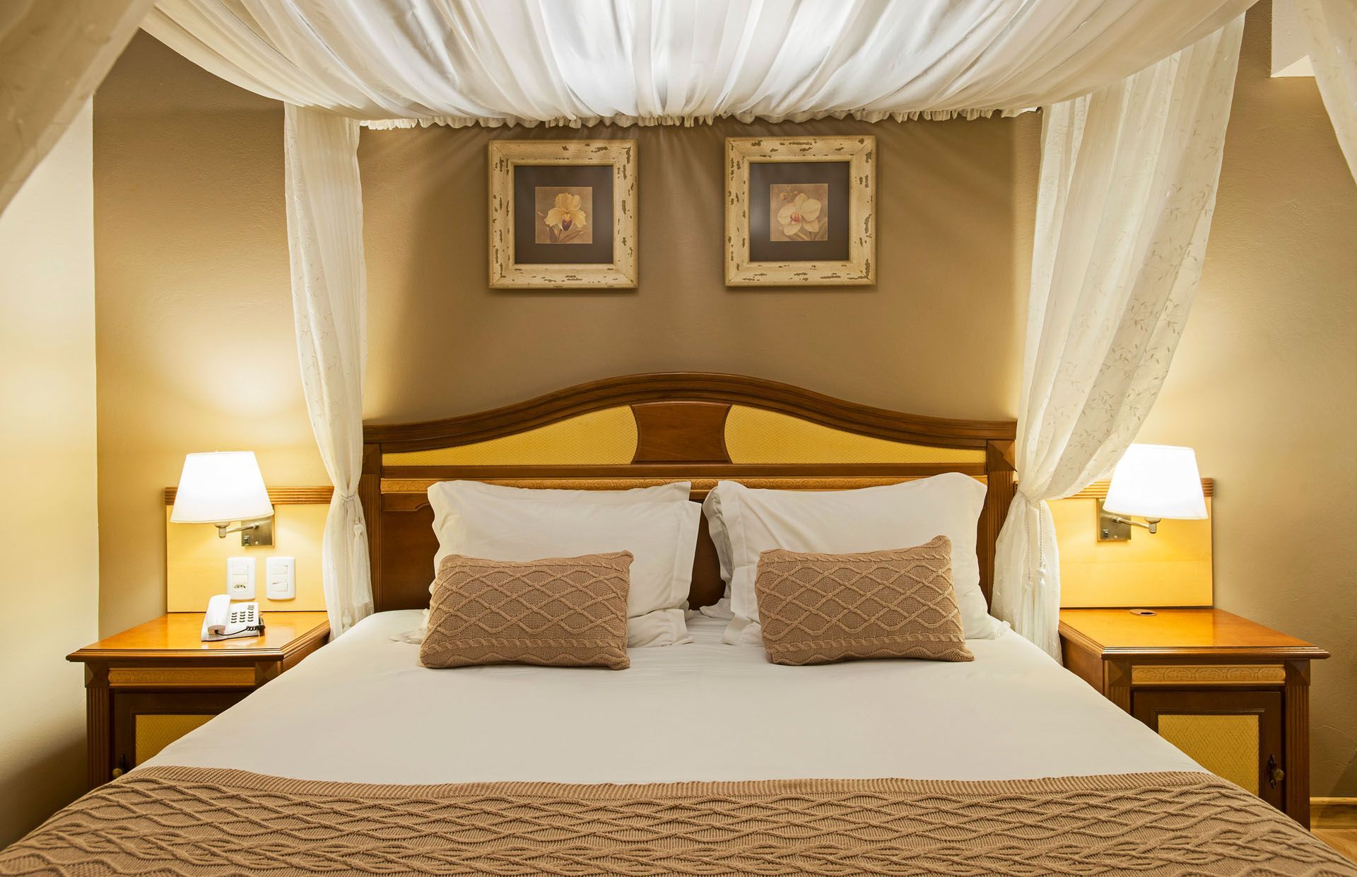 Quarto aconchegante com cama de dossel, cortinas brancas, abajures e decoração em tons de bege quente.