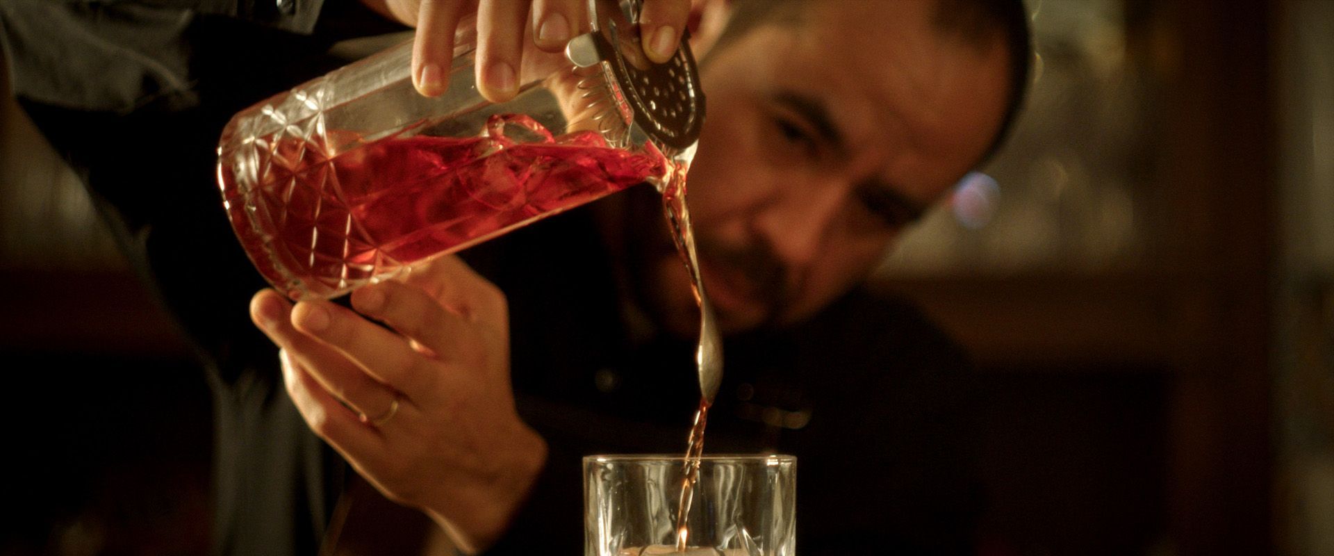 O barman serve um coquetel vermelho de uma coqueteleira para um copo atrás do balcão.