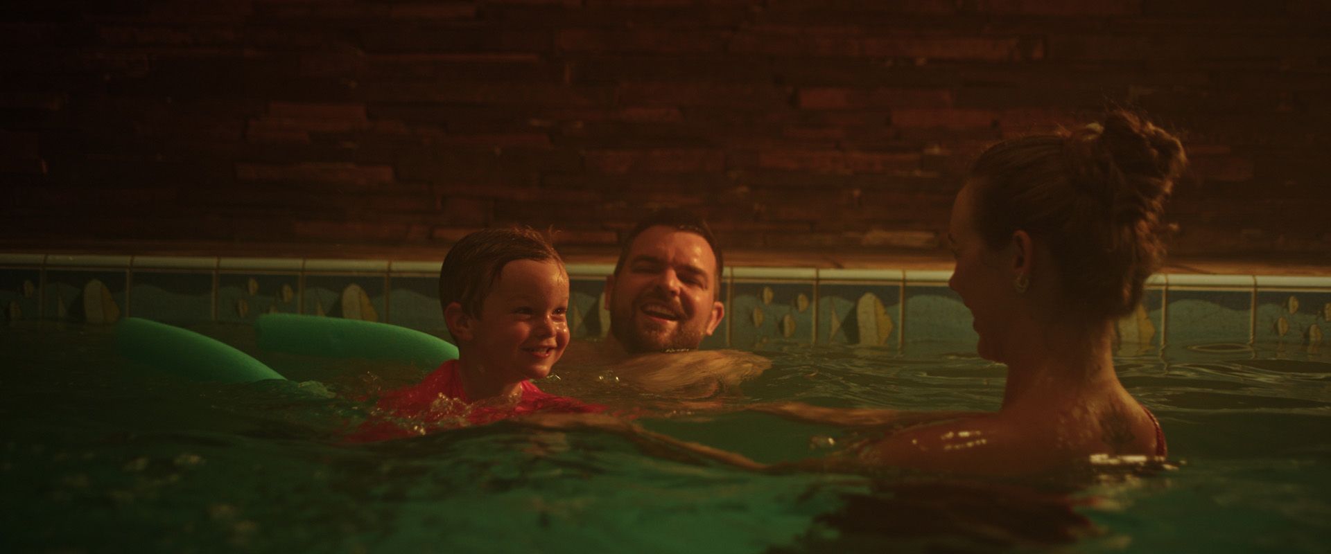 Pessoas relaxando em uma piscina coberta com pouca luz, frente a frente na água morna.