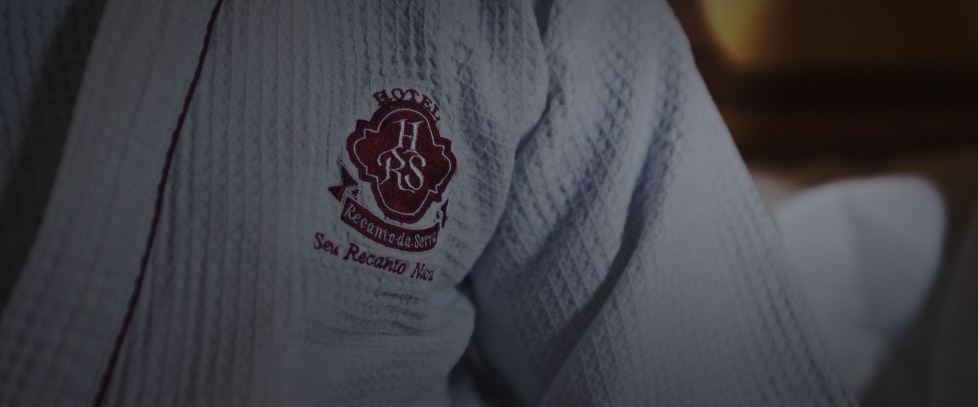 Detalhe de um suéter de tricô branco com um brasão bordado em tom bordô no peito.