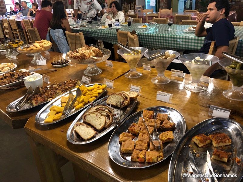 Buffet do Café Colonial Della Nonna – Família Foss com pães caseiros, bolos, tortas salgadas e salgados quentes em travessas.
